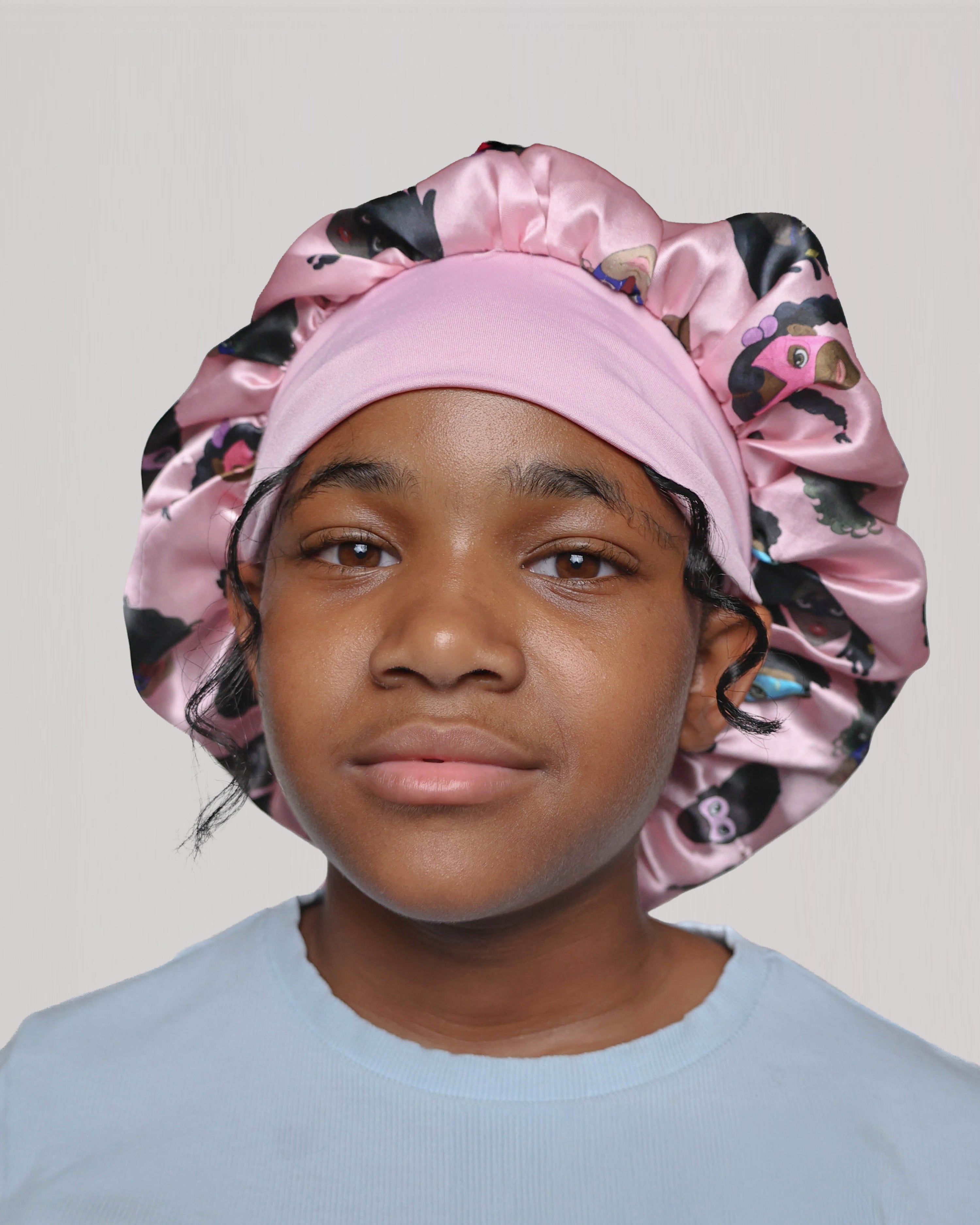 Child wearing a pink bonnet with black and brown superhero's on a plain background