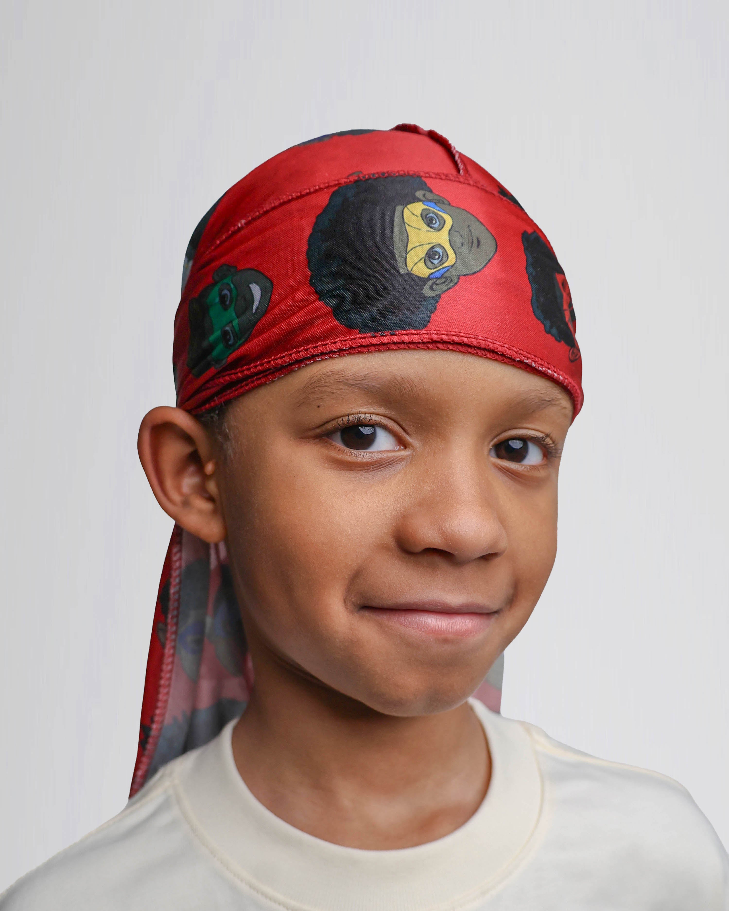 Child wearing a red durag with black and brown superhero's on a plain background