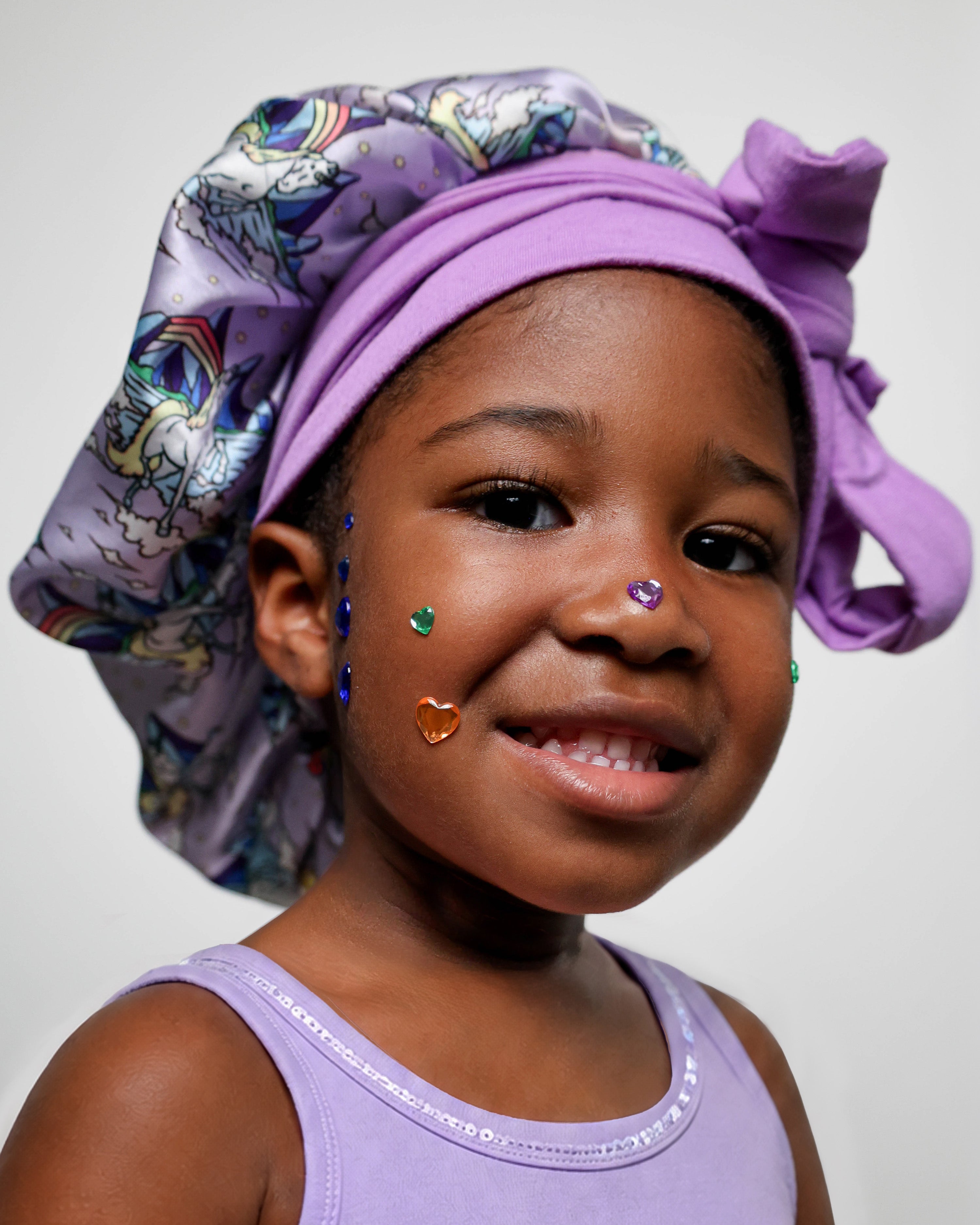 Child wearing a purple unicorn patterned bonnet on a plain background