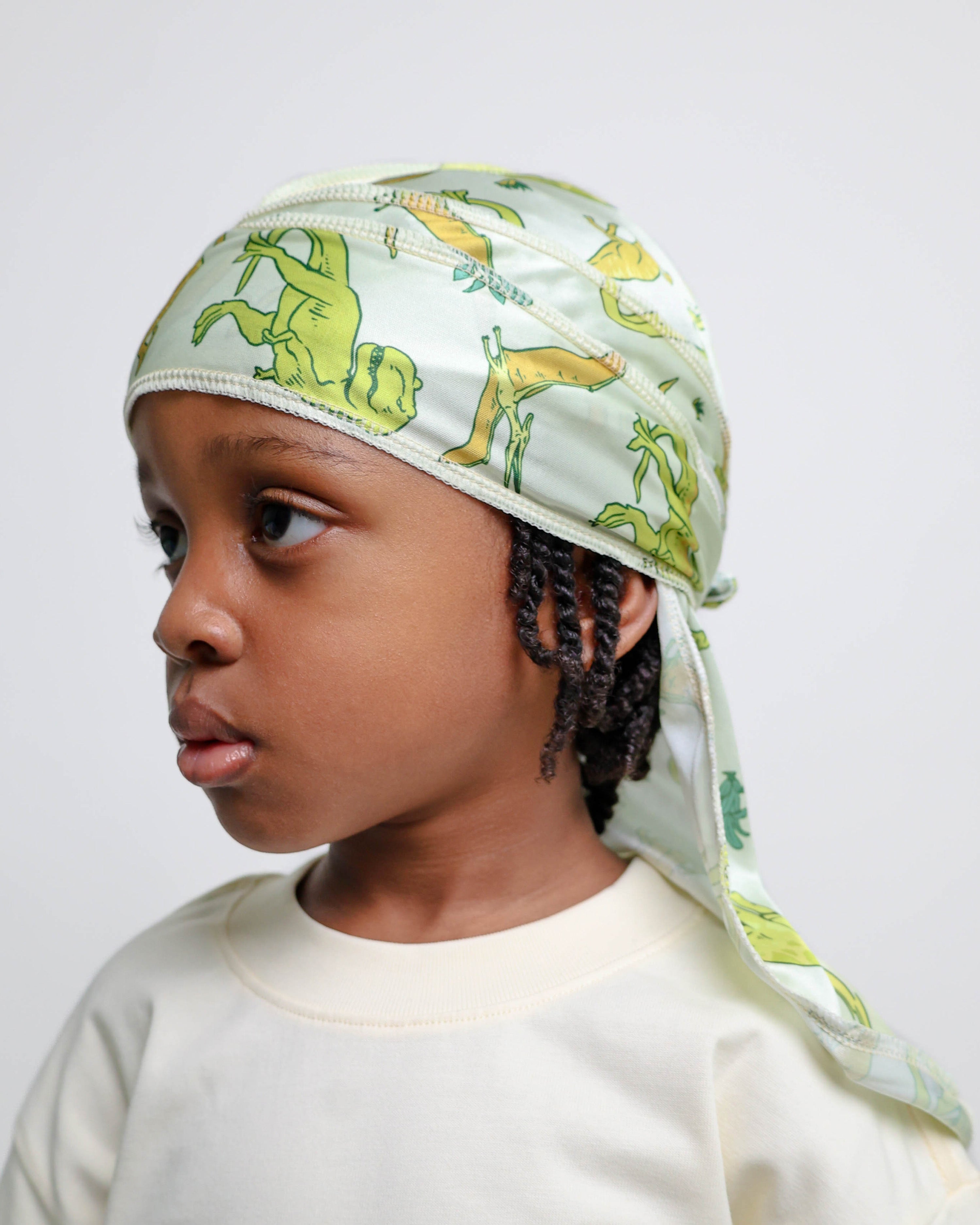 Child wearing a dinosaur patterned durag on a plain background