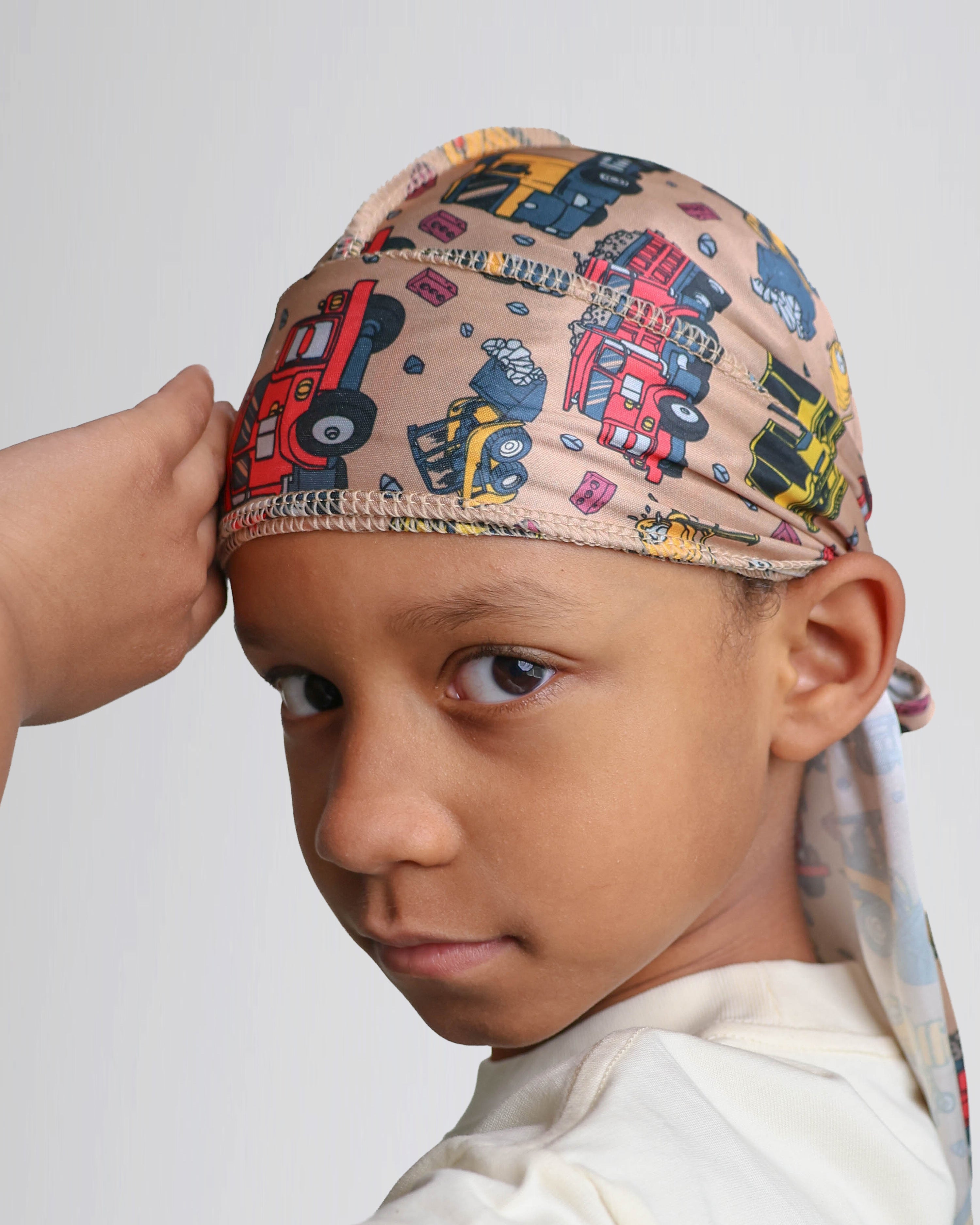 Child wearing a construction truck patterned durag on a plain background
