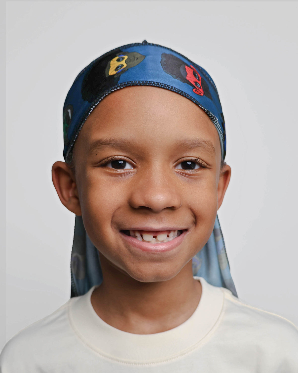 Smiling boy in the blue MY HERO kids satin durag with Black and brown superhero print, front view